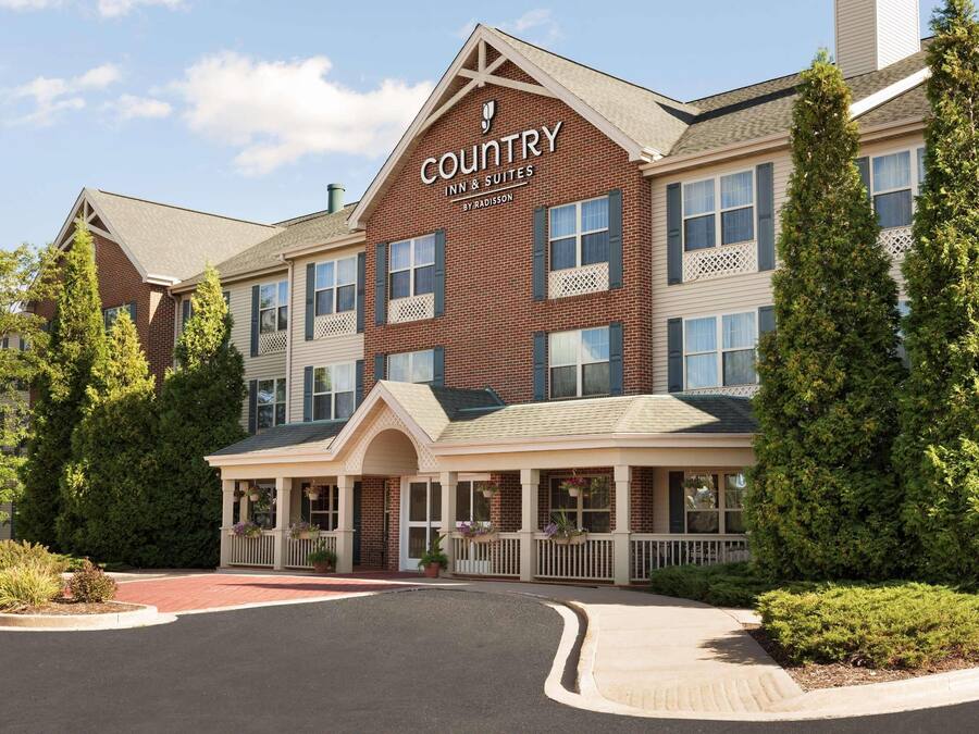 A Country Inn & Suites building with a brick facade, multiple windows, and a covered front porch with hanging flower baskets.
