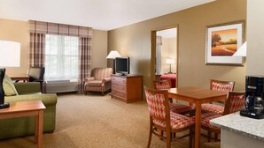 A hotel room with a green sofa, a striped armchair, a wooden table with a coffee maker, a TV, and a painting on the wall.