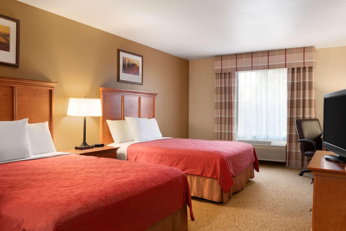 A hotel room with two beds, a desk, a chair, a television, and a window with curtains.