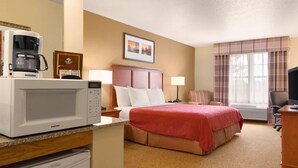 Habitación de hotel con cama, microondas, cafetera, escritorio, silla y ventana con cortinas.