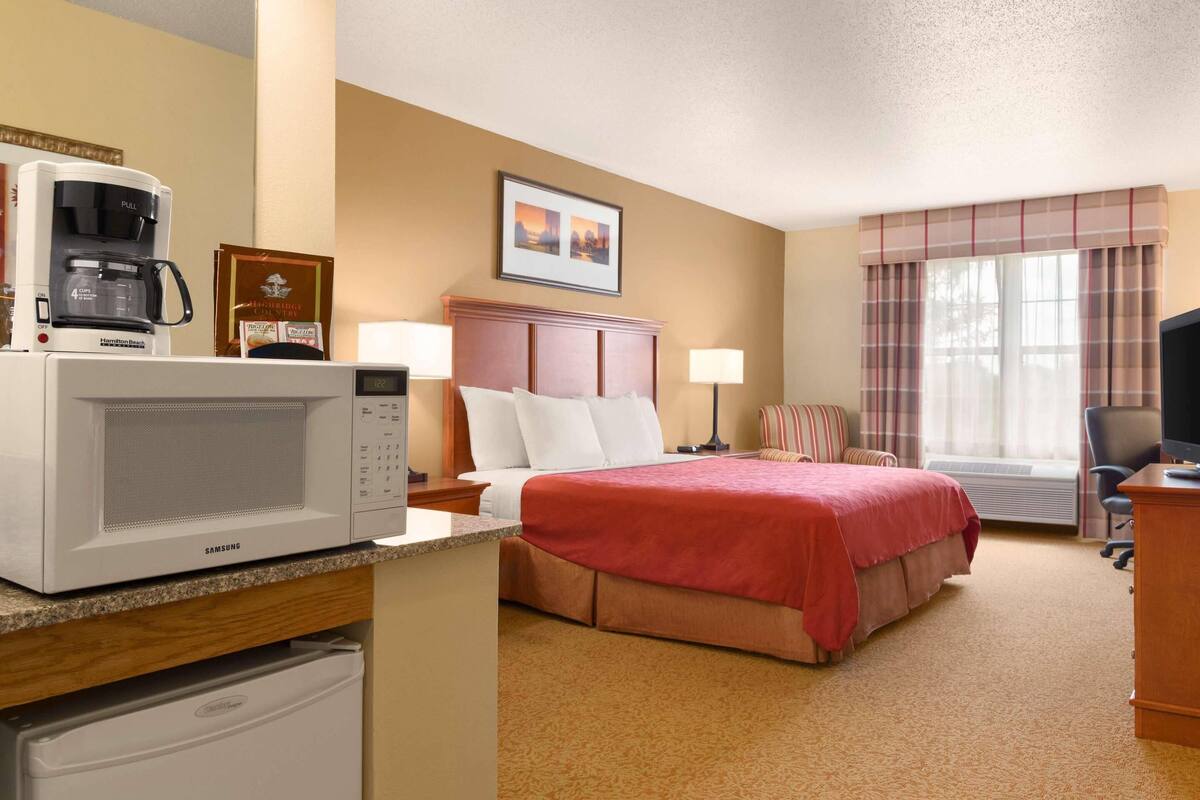 Une chambre d’hôtel équipée d’un lit, d’un four à micro-ondes, d’une machine à café, d’un bureau, d’une chaise et d’une fenêtre avec des rideaux.