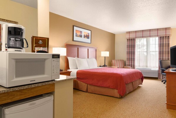 A hotel room with a bed, a microwave, a coffee maker, a desk, a chair, and a window with curtains.