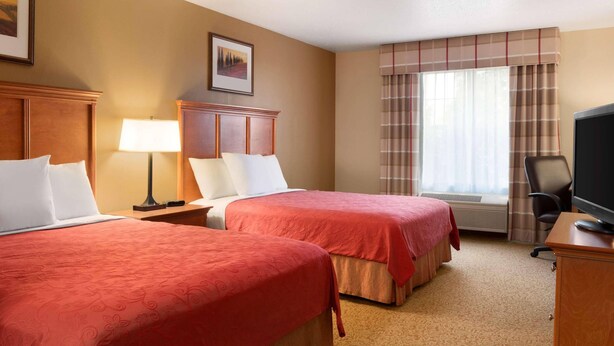 A hotel room with two beds, a desk, a chair, a TV, and a window with curtains.