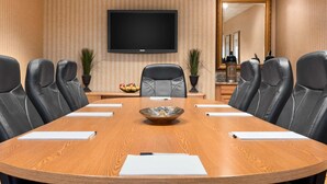 Una sala de conferencias con una gran mesa de madera, sillas de cuero negro, un televisor de pantalla plana y un cuenco decorativo en el centro.