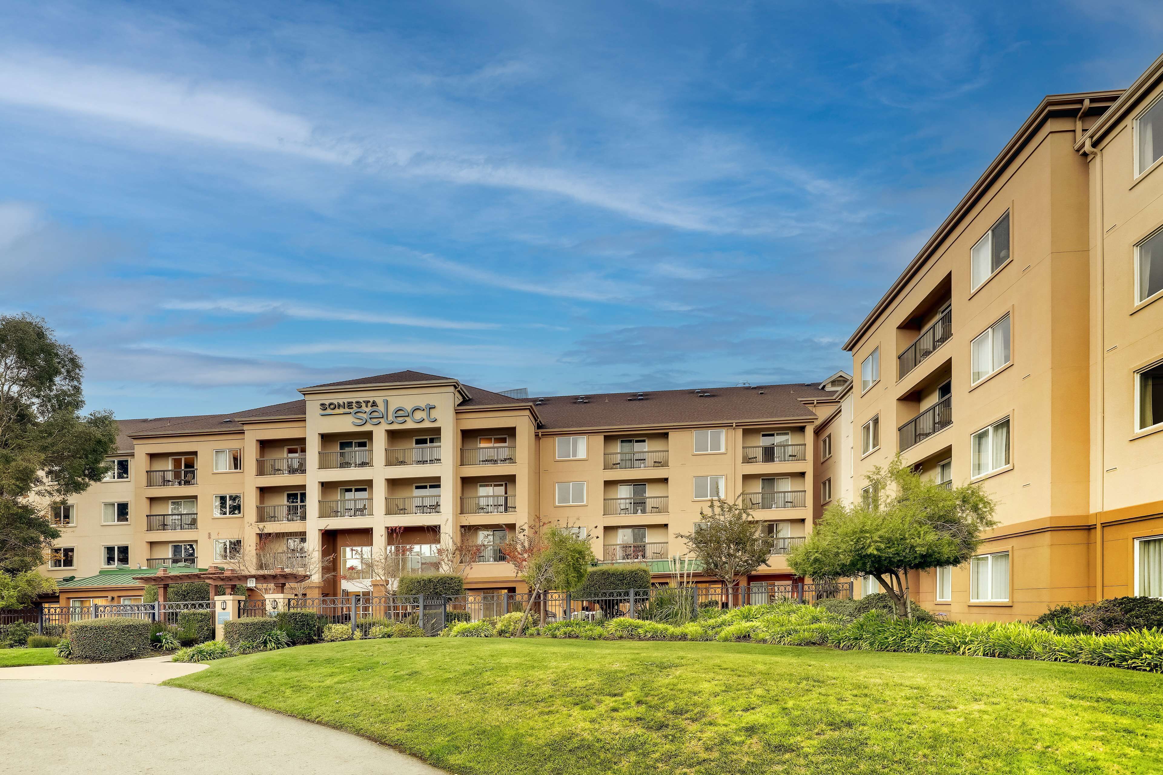 A multi-story hotel with balconies, a well-maintained lawn, and a clear sky.