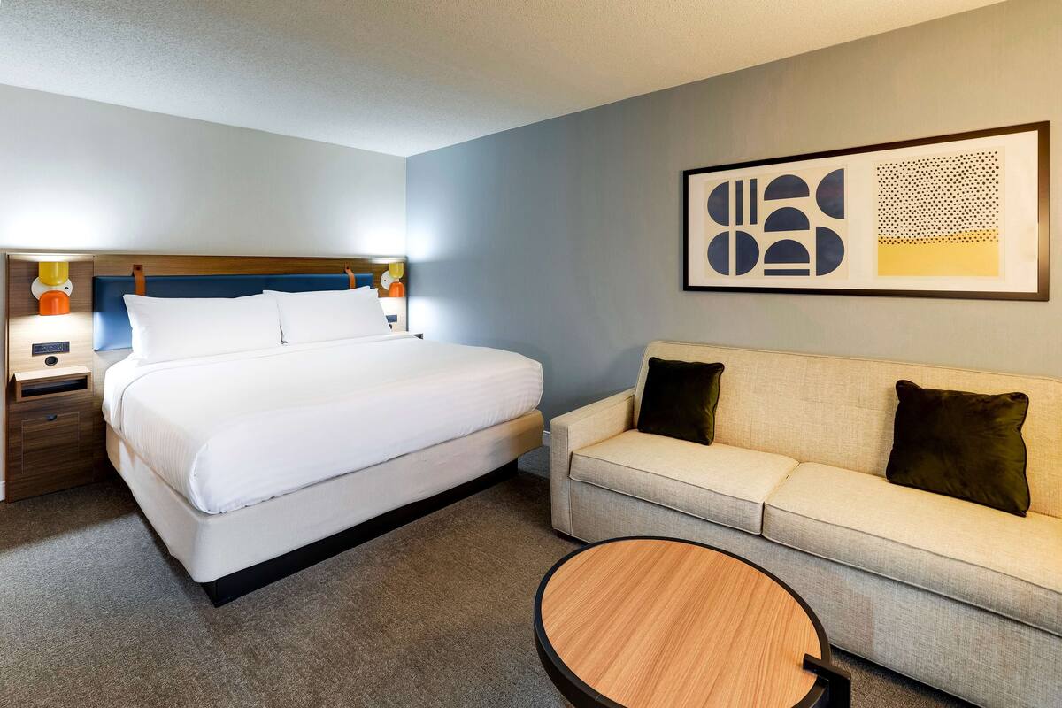 Una habitación de hotel con cama, sofá, una mesita redonda y una obra de arte en la pared.