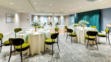 A conference room with round tables, green chairs, and white tablecloths.