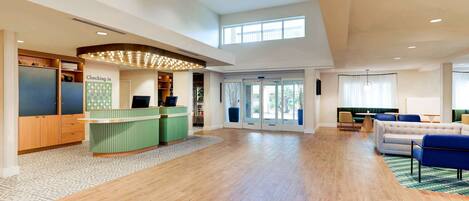 A spacious lobby with a reception desk, a seating area with a sofa and chairs, and a large window providing natural light.
