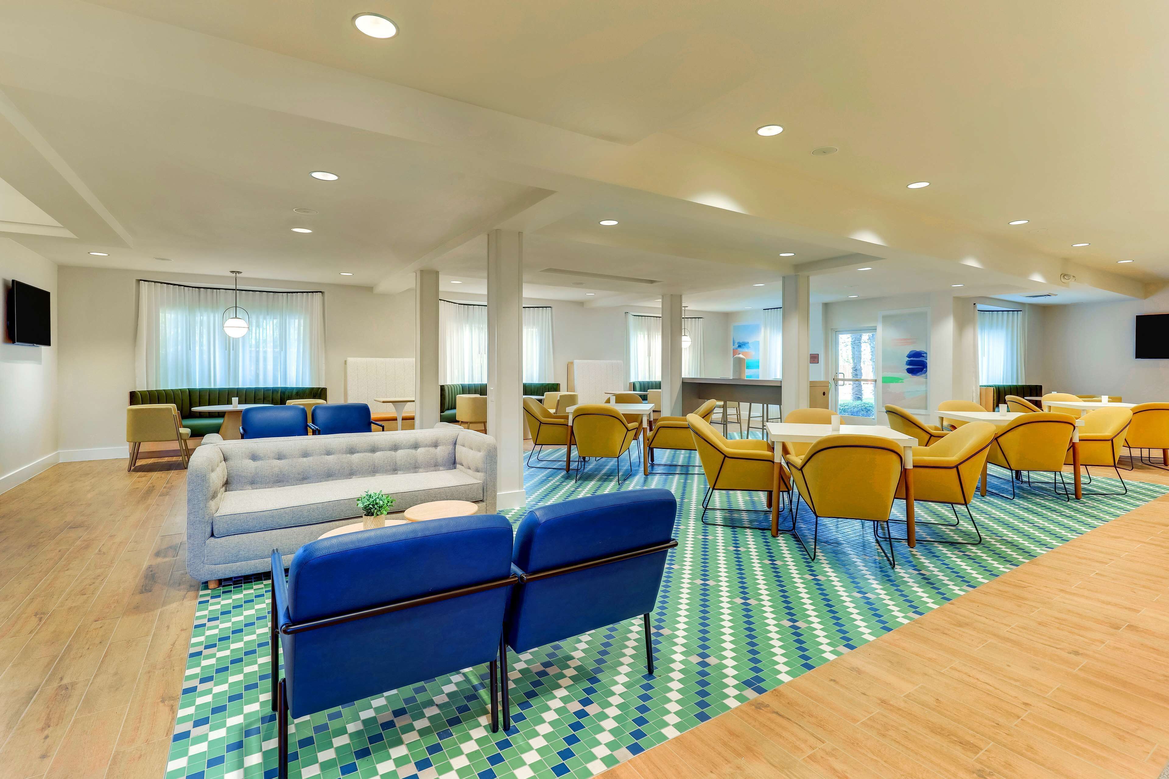 A modern hotel lobby with a sofa, blue chairs, yellow tables, and a patterned floor.