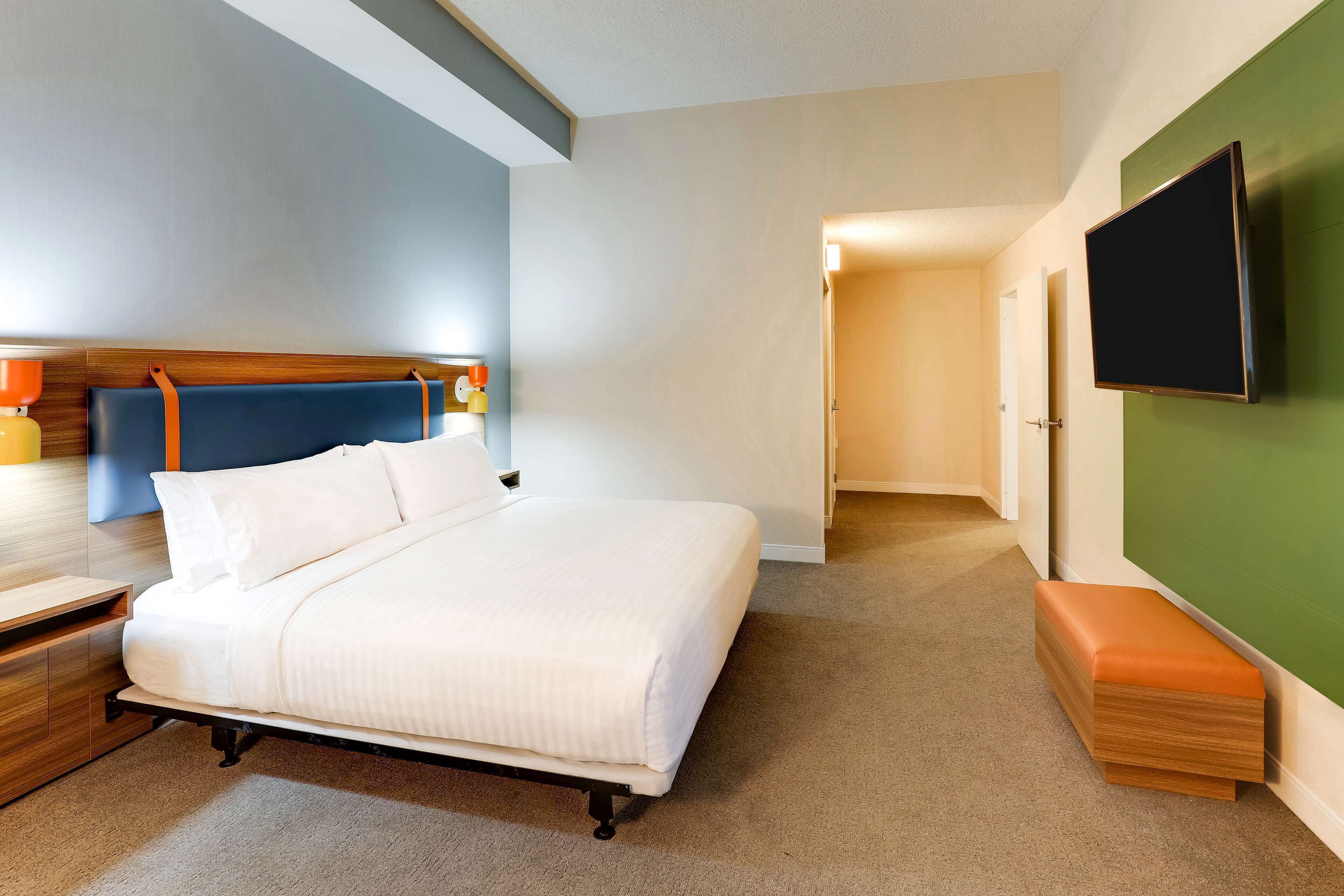 Quarto de hotel com cama, mesa de cabeceira e televisão de tela plana na parede.