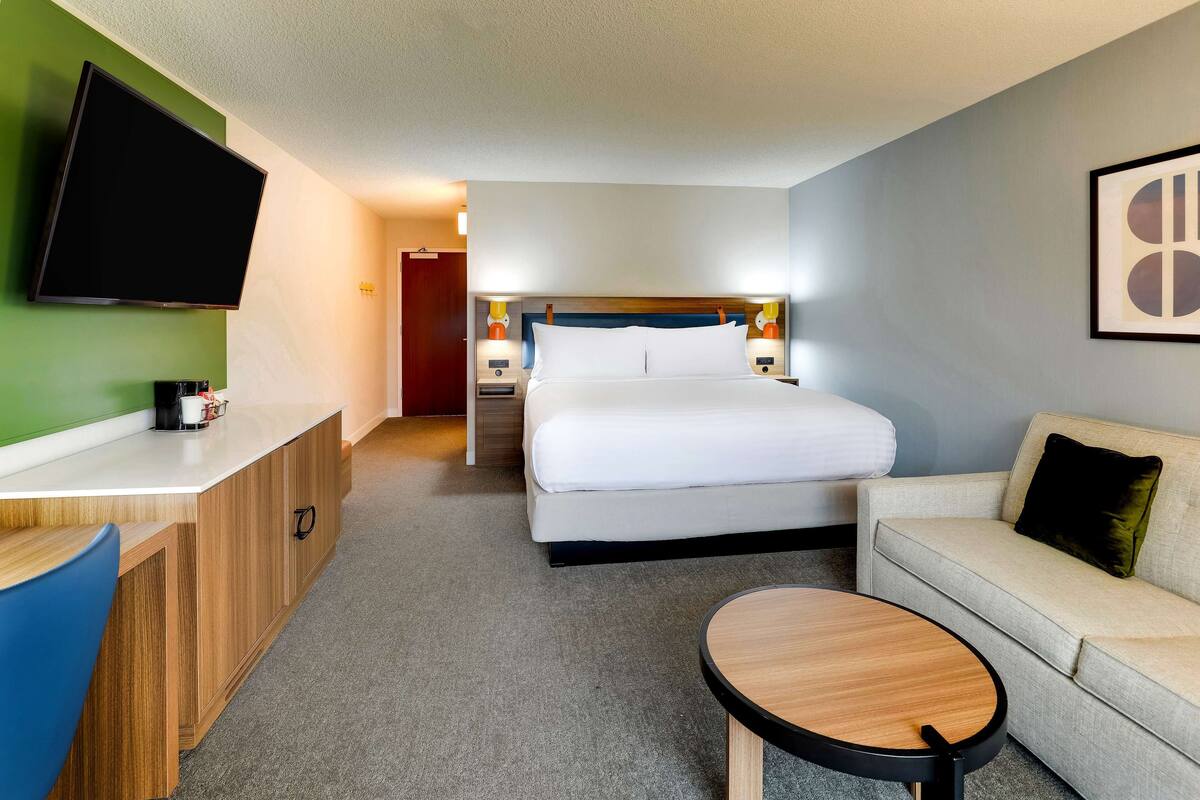 Habitación de hotel con cama, escritorio, silla, mesita, televisor y sofá.