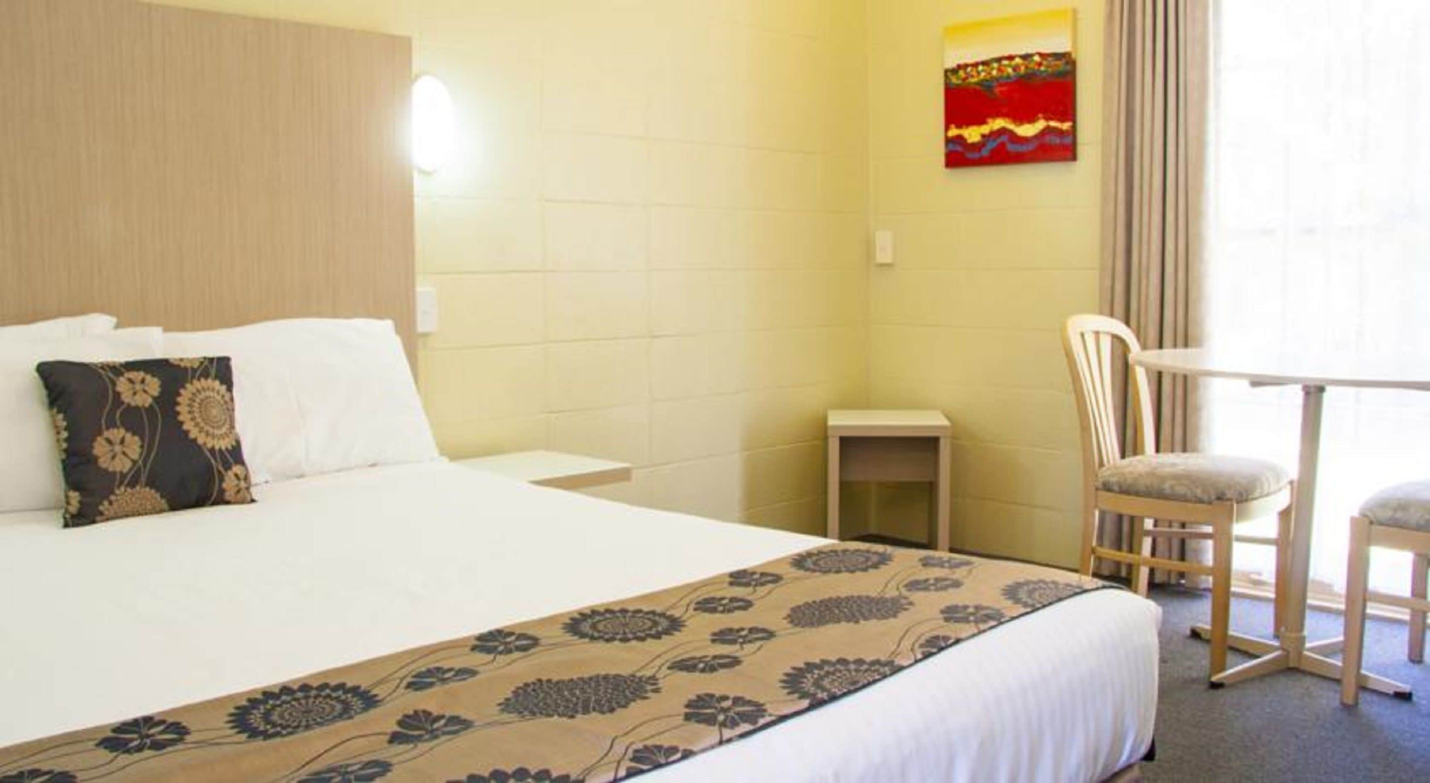 A hotel room with a large bed, a bedside table, a chair, and a small table.