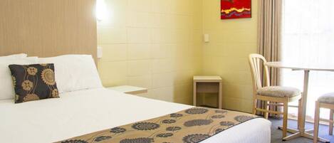 A hotel room with a large bed, a bedside table, a chair, and a small table.