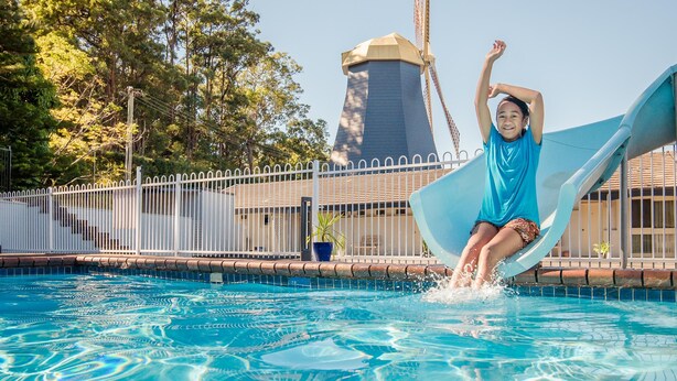 A person sliding into a pool with a water tower in the background. - Coffs Windmill Motel (Coffs Harbour)