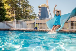 A person sliding into a pool with a water tower in the background. - Coffs Windmill Motel (Coffs Harbour)