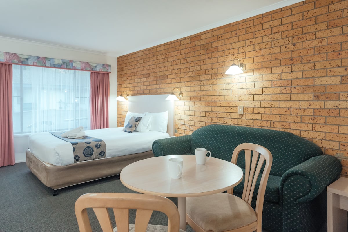 A hotel room with a bed, a green sofa, a round table, and a brick wall.