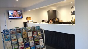 A reception area with a counter, a television mounted on the wall, and a rack of brochures. - Coffs Windmill Motel (Coffs Harbour)
