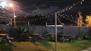 An outdoor area with picnic tables, string lights, and a grassy field. - Coffs Windmill Motel (Coffs Harbour)