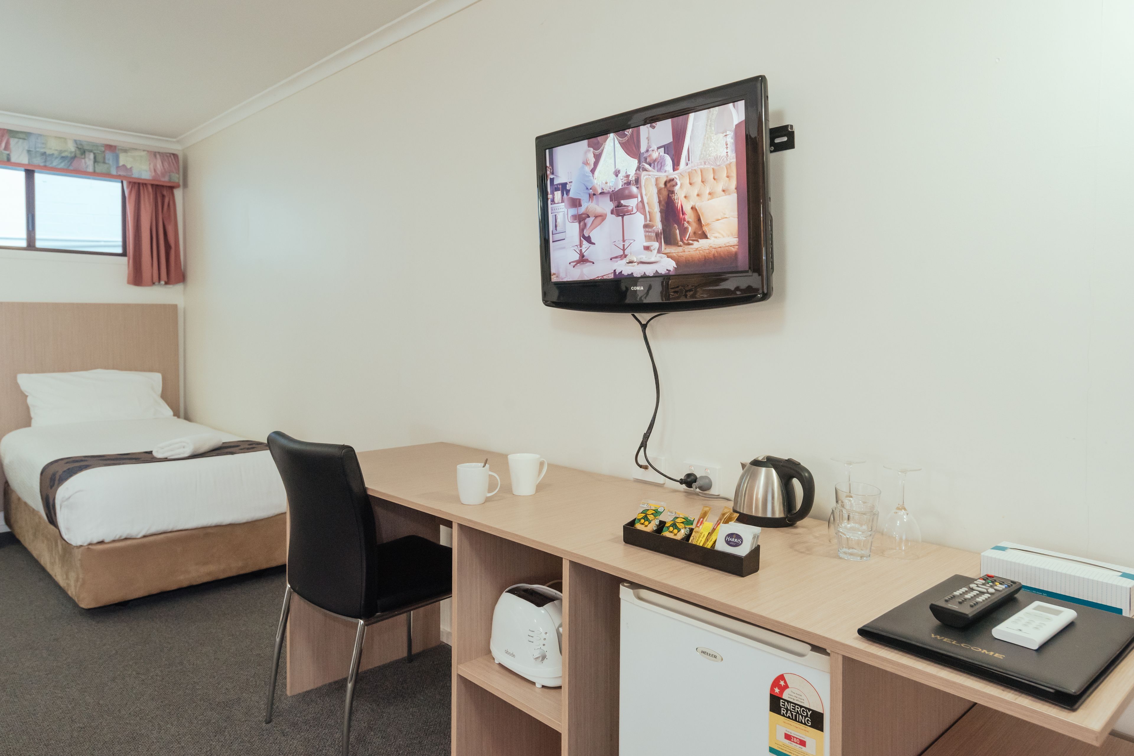 Habitación de hotel con cama, escritorio con computadora, televisor y un mini refrigerador.