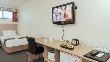 Habitación de hotel con cama, escritorio con computadora, televisor y un mini refrigerador.