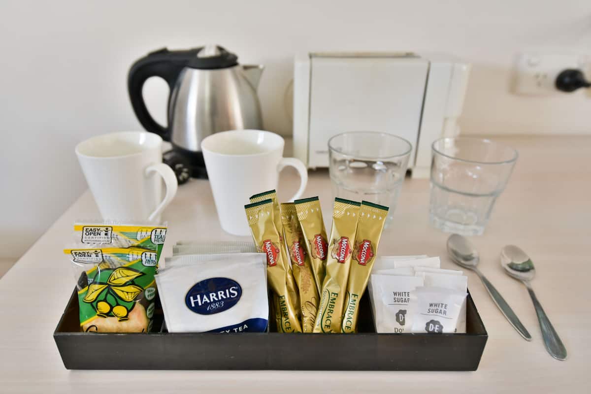 A tray with tea bags, sugar packets, and a coffee pot on a table.
