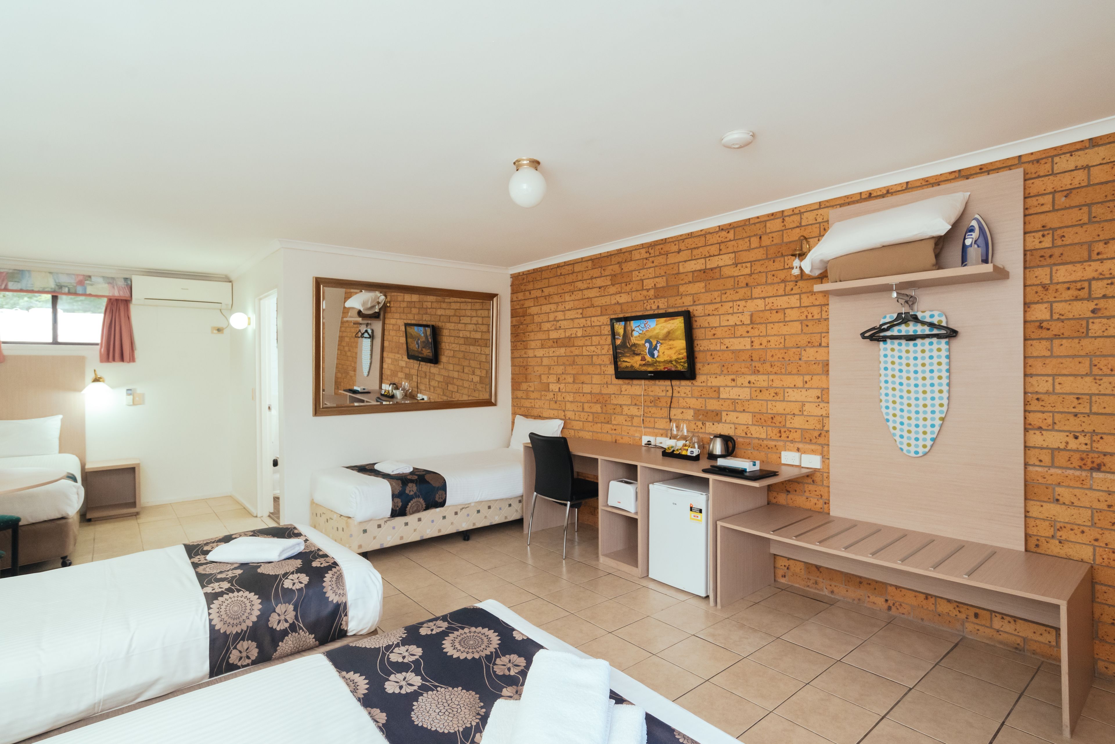 Habitación de hotel con dos camas, un escritorio, un refrigerador pequeño, un tendedero y una pared de ladrillo.