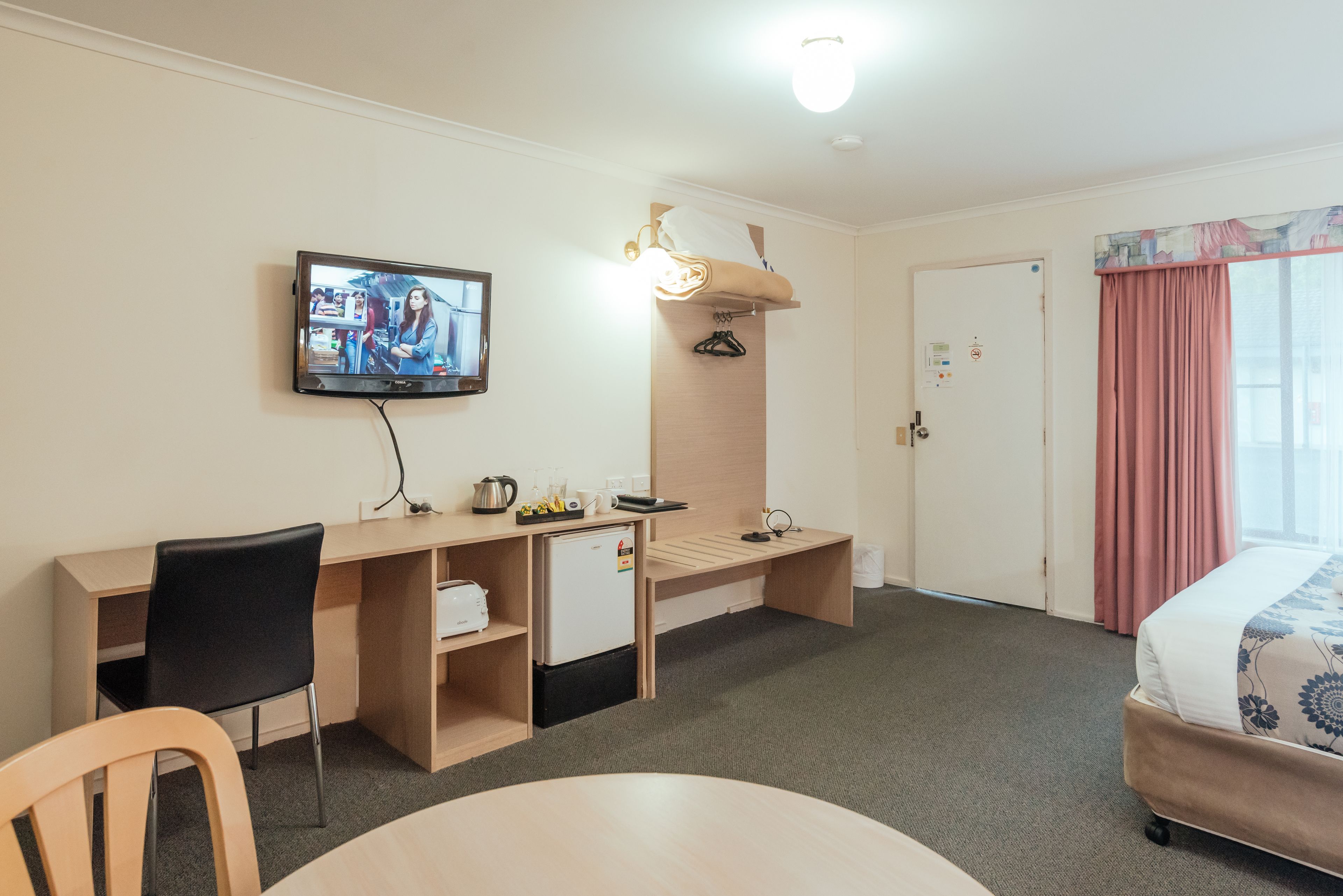 Una habitación de hotel con cama, escritorio, silla, televisor, armario y puerta.