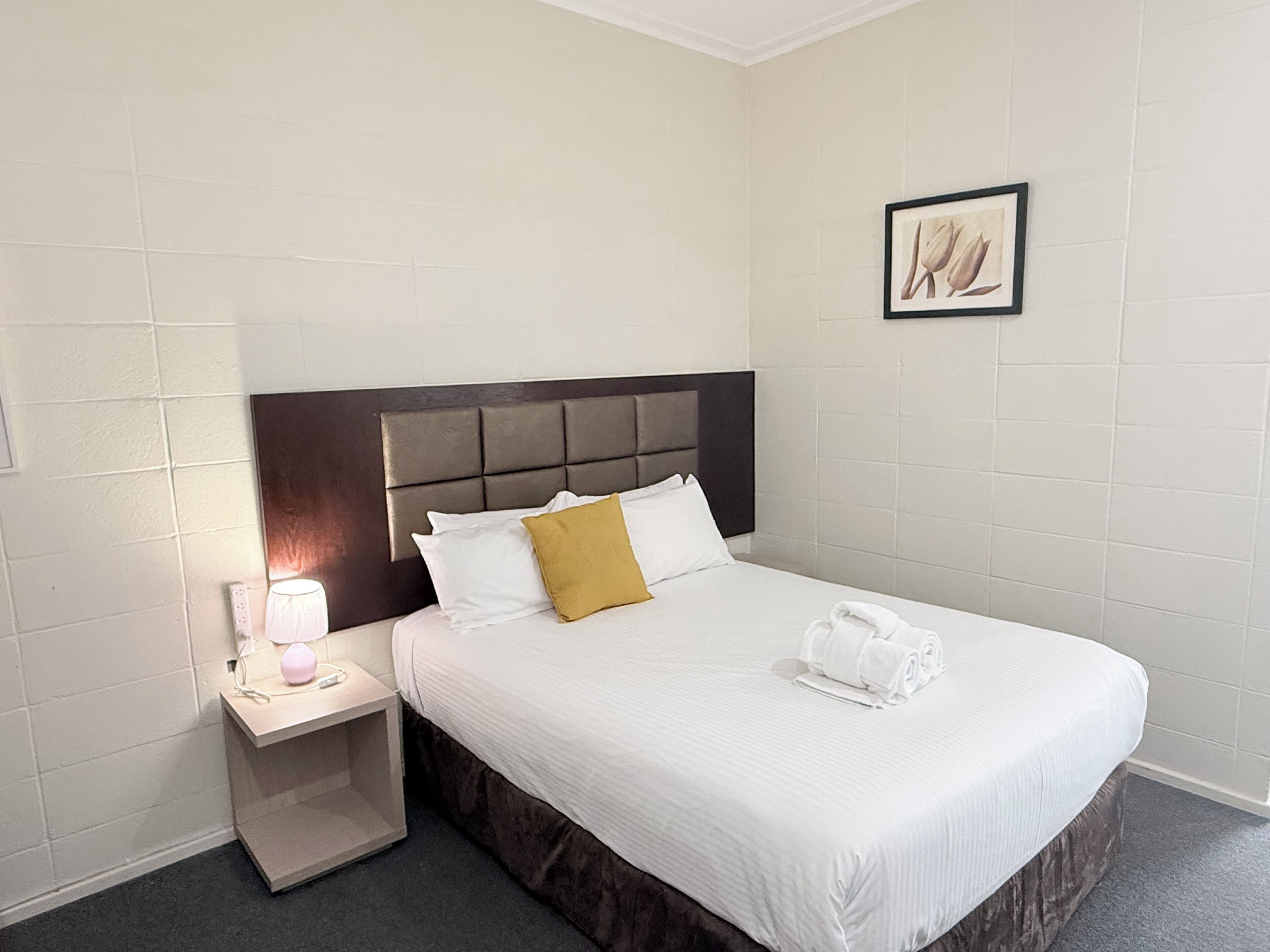 A hotel room with a bed, a nightstand, a lamp, and a framed picture on the wall.
