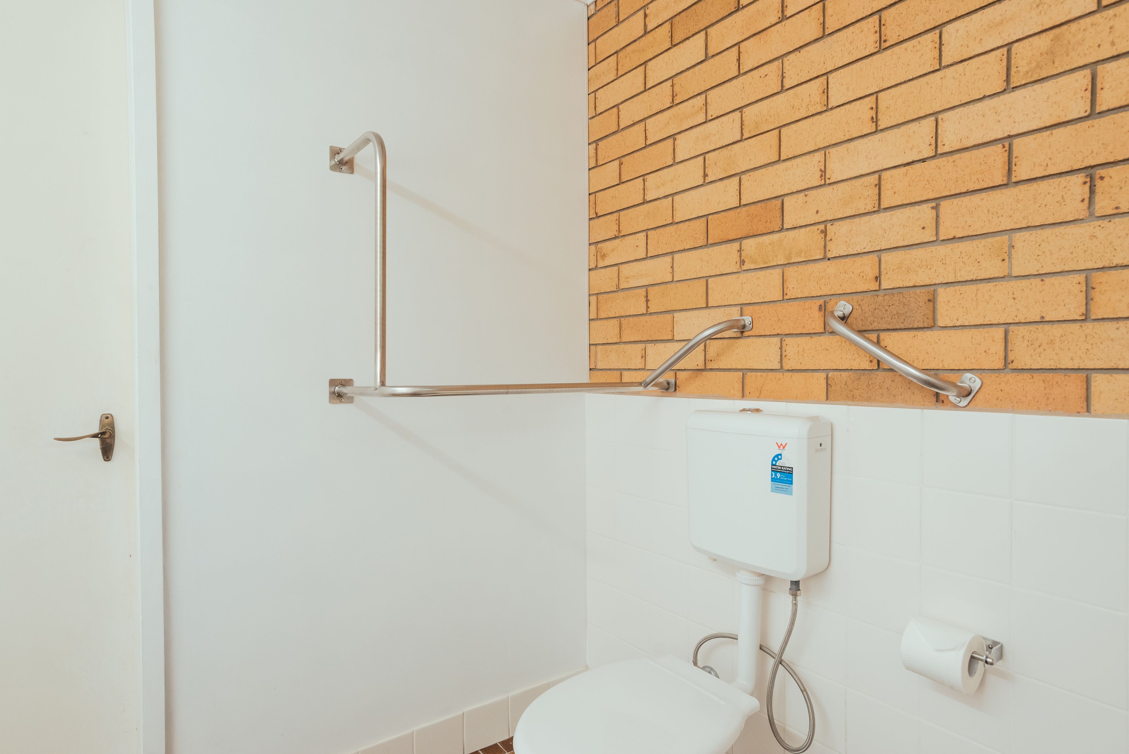 A bathroom with a white toilet, a white sink, a white shower, and a brick wall.