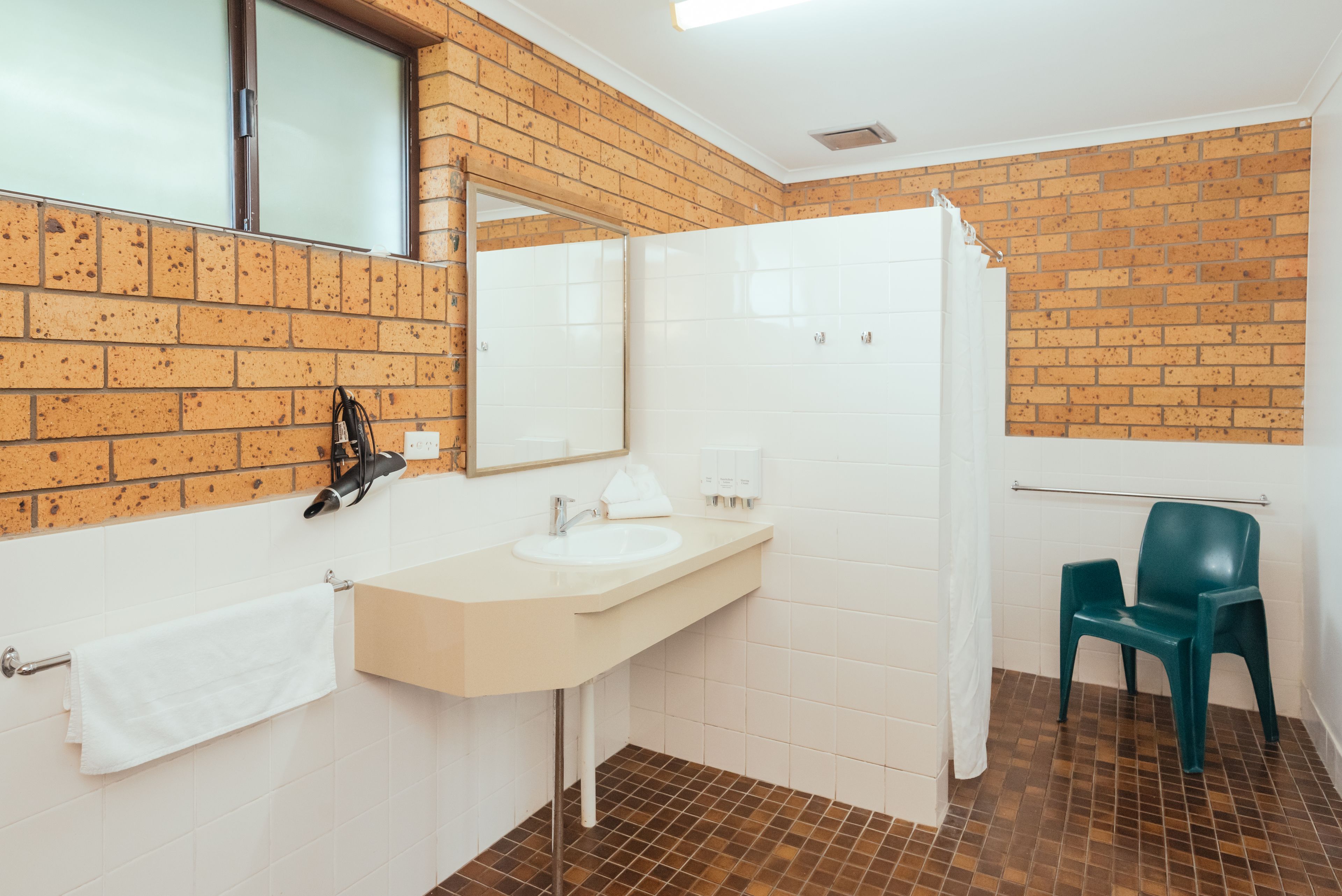 A bathroom with a white sink, a mirror, a towel rack, a shower curtain, and a green chair.