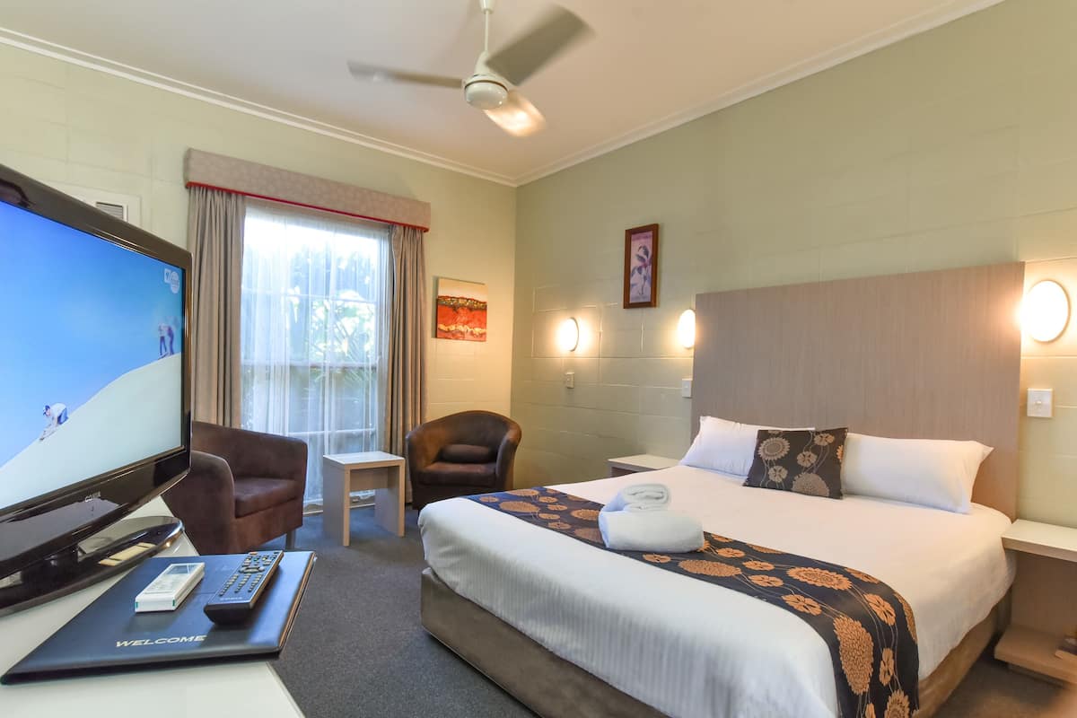 A hotel room with a bed, a TV, a chair, a desk, and a ceiling fan.