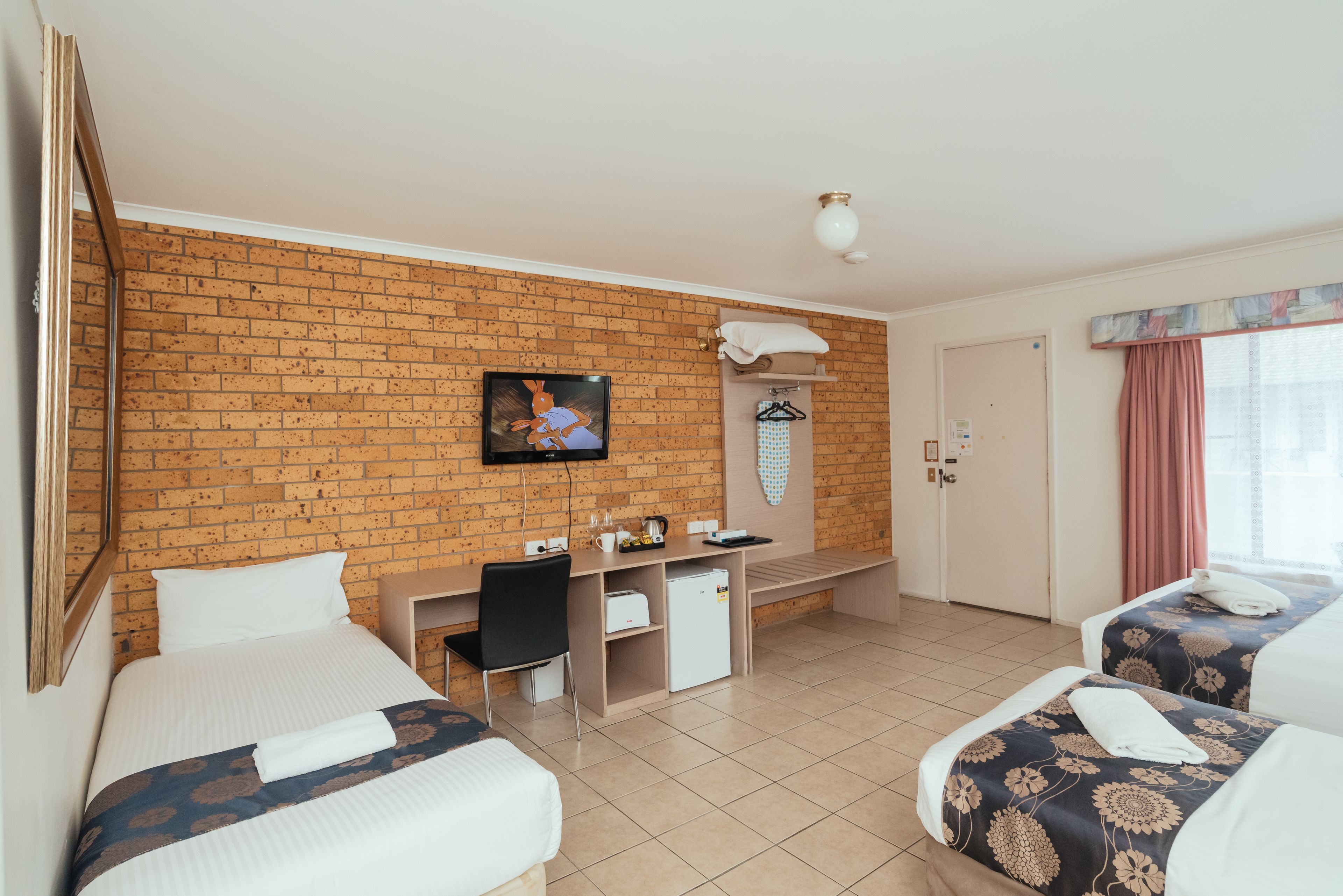 Une chambre d’hôtel avec deux lits, un bureau, une télévision et un mur en briques.