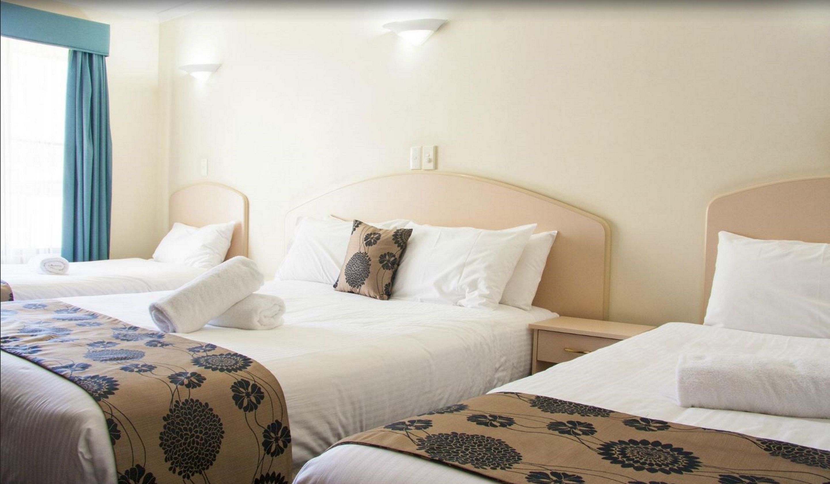 A hotel room with two single beds, each with a headboard, bedside tables, and a window with curtains.