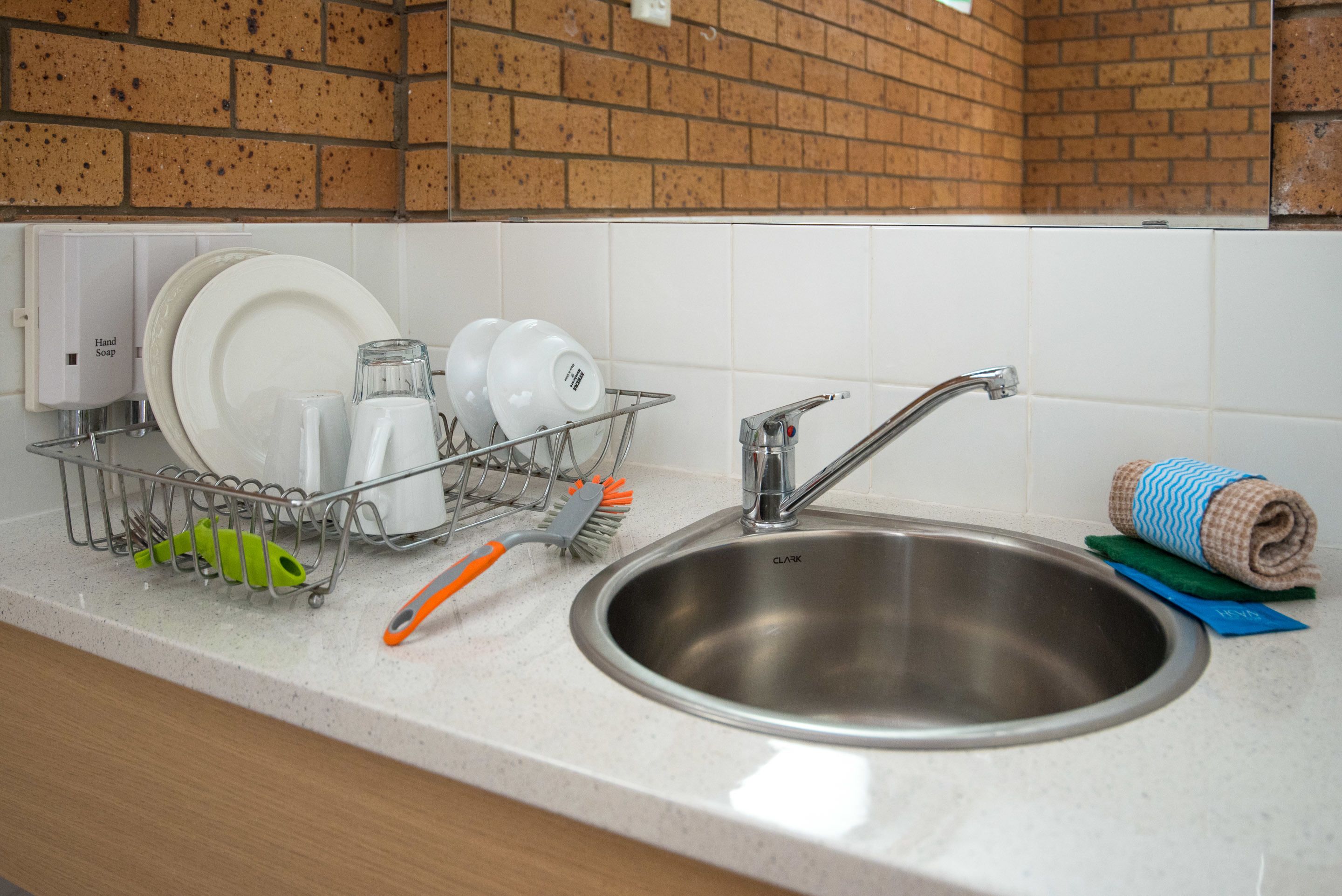 A stainless steel sink with a faucet, a dish rack with dishes and a brush, and a towel on the counter.