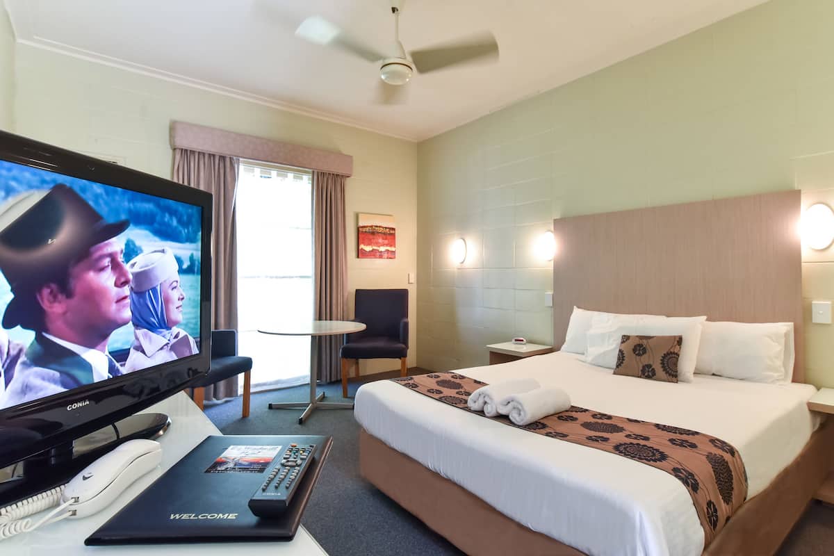 A hotel room with a bed, a TV, a desk with a phone, a chair, and a small table.