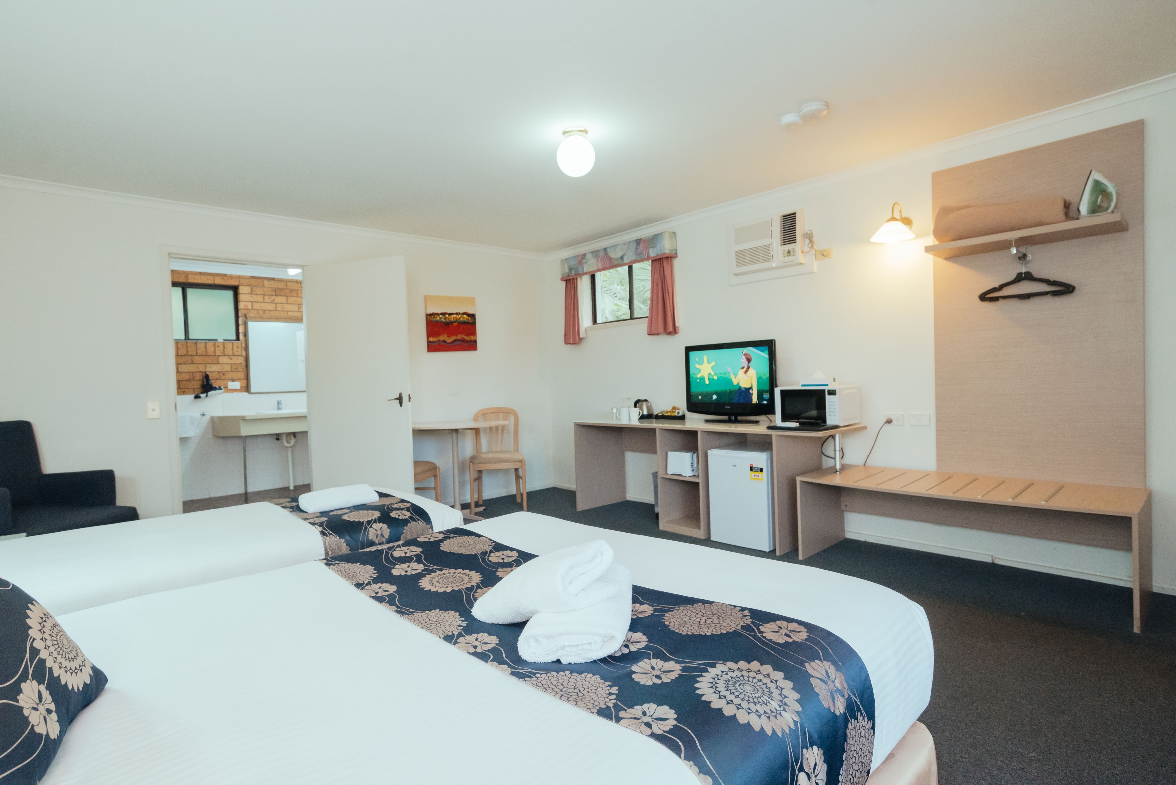 A hotel room with two beds, a desk with a computer, a television, and a small seating area.
