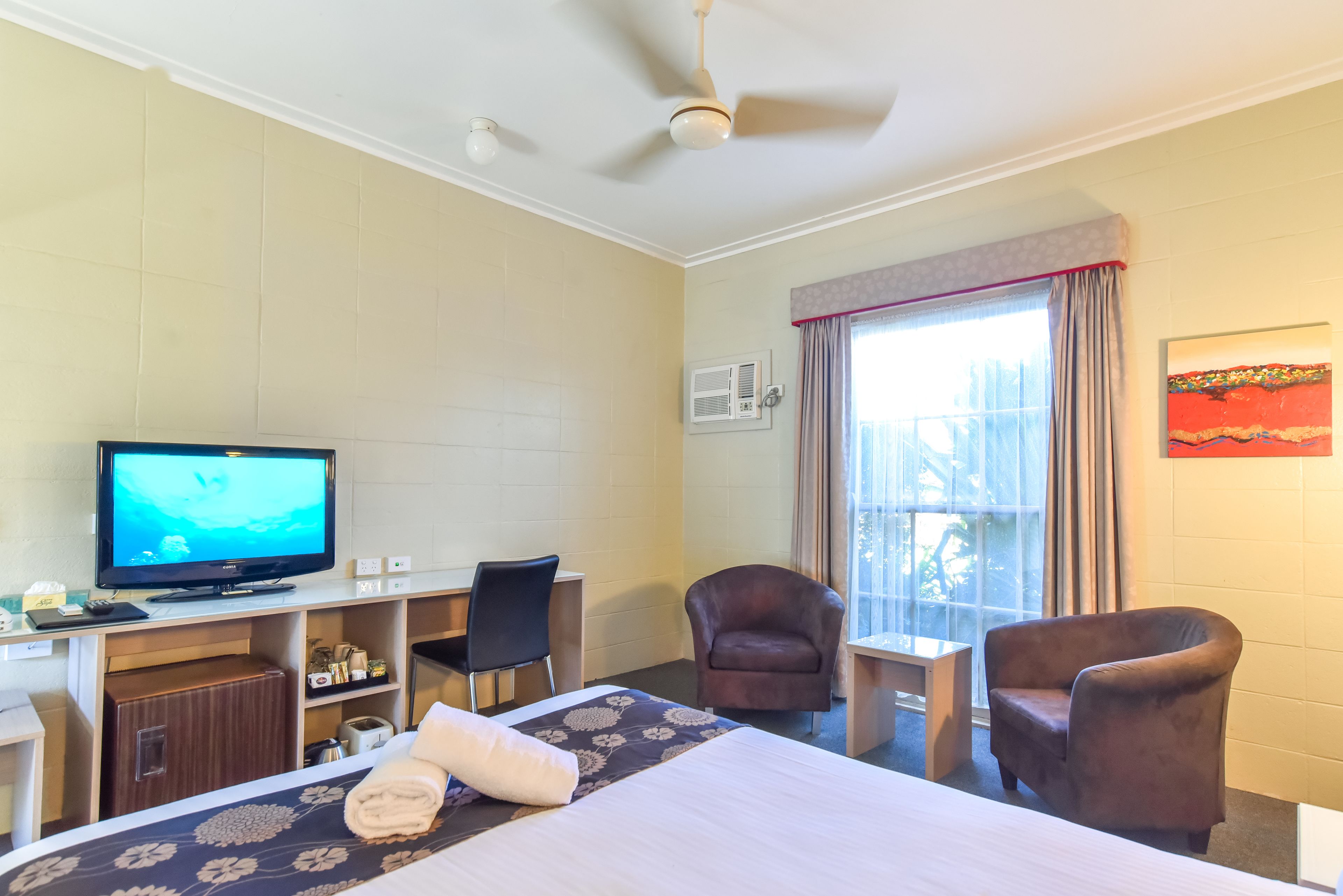 A hotel room with a bed, a desk, a chair, a television, and a window with curtains.