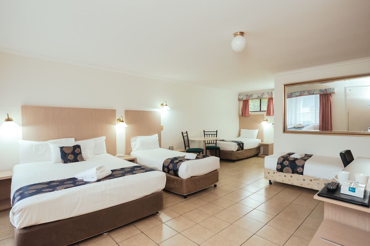 A hotel room with three beds, a desk, and a chair.