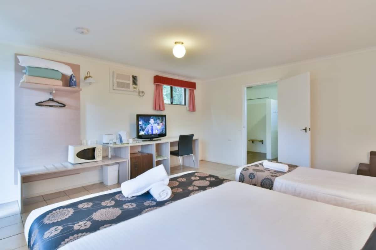 A hotel room with two beds, a TV, a desk with a computer, a chair, and a wardrobe.