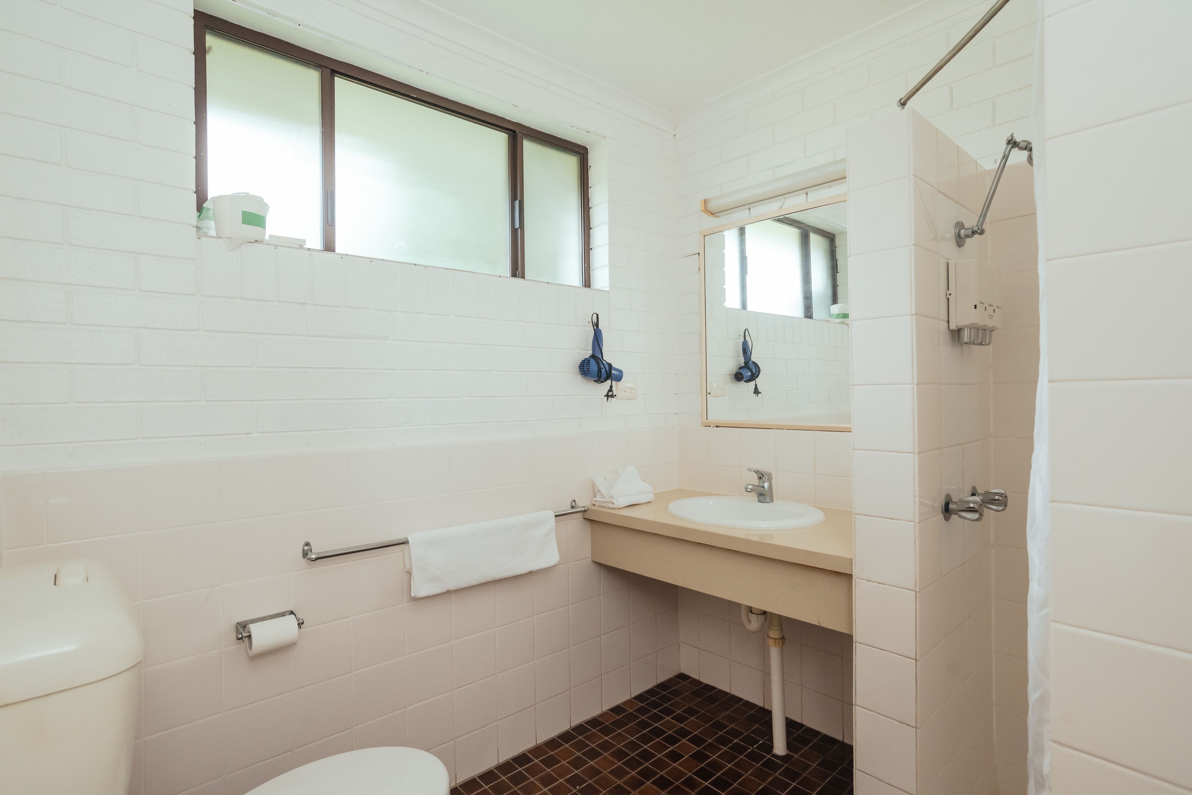 A bathroom with a white toilet, a sink with a mirror above it, a towel rack, and a shower area.