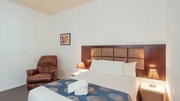 A hotel room with a bed, a brown leather chair, a nightstand with a lamp, and a framed picture on the wall.