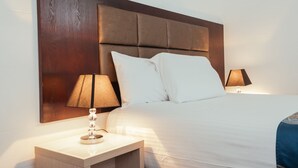 A neatly made bed with white linens, a wooden headboard, and two bedside lamps. - Coffs Windmill Motel (Coffs Harbour)