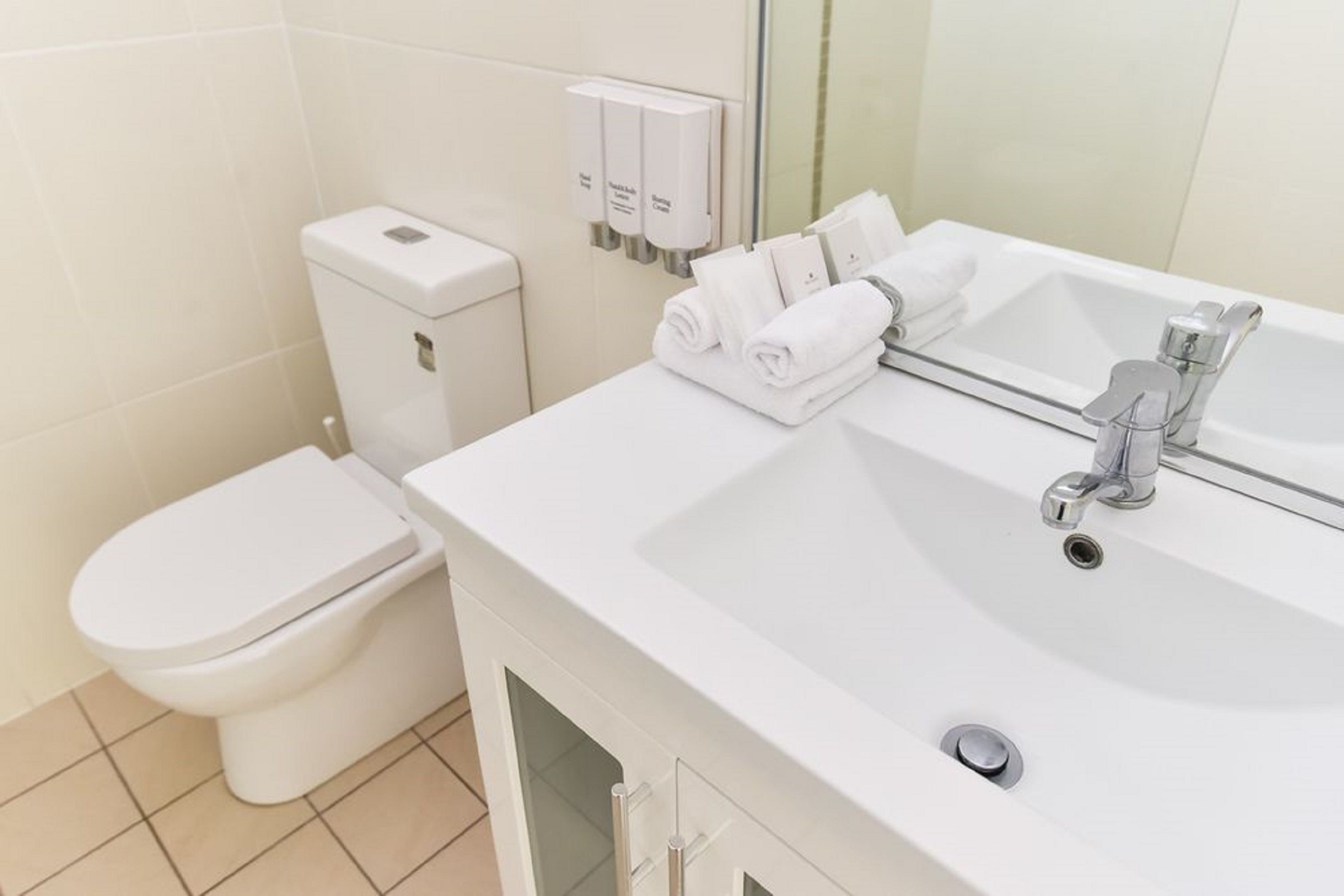 A modern bathroom with a toilet, a sink with a mirror, and a towel dispenser.