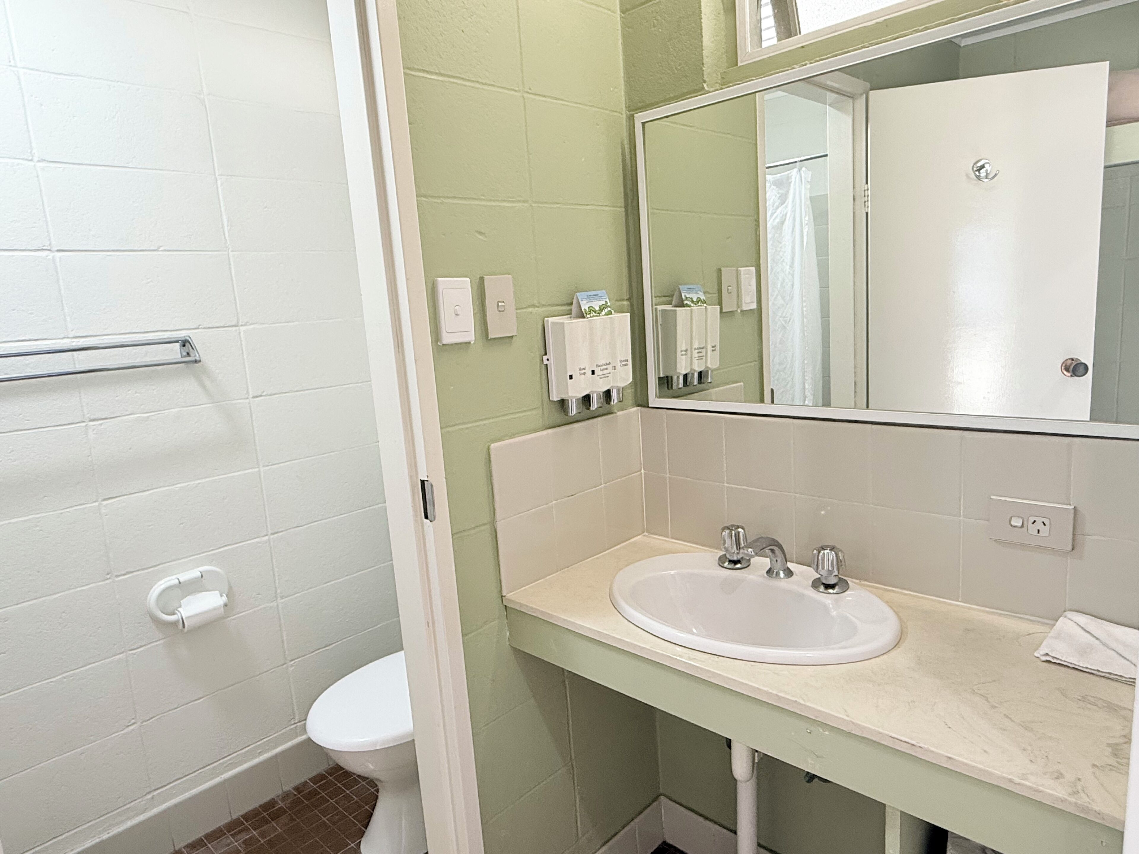 Un baño con inodoro blanco, lavamanos con espejo y un perchero para toallas.