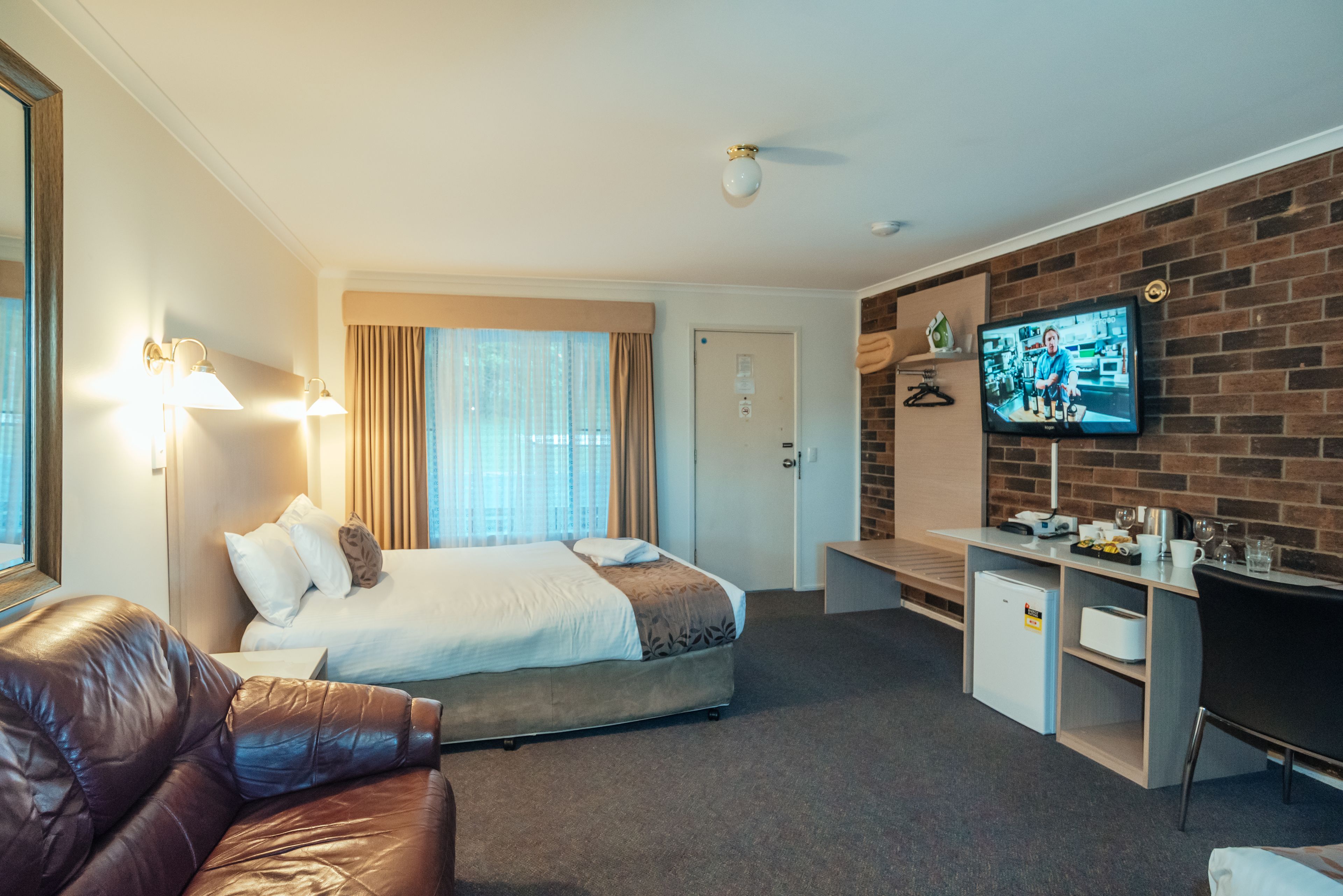 A hotel room with a bed, a desk, a television, and a leather sofa.