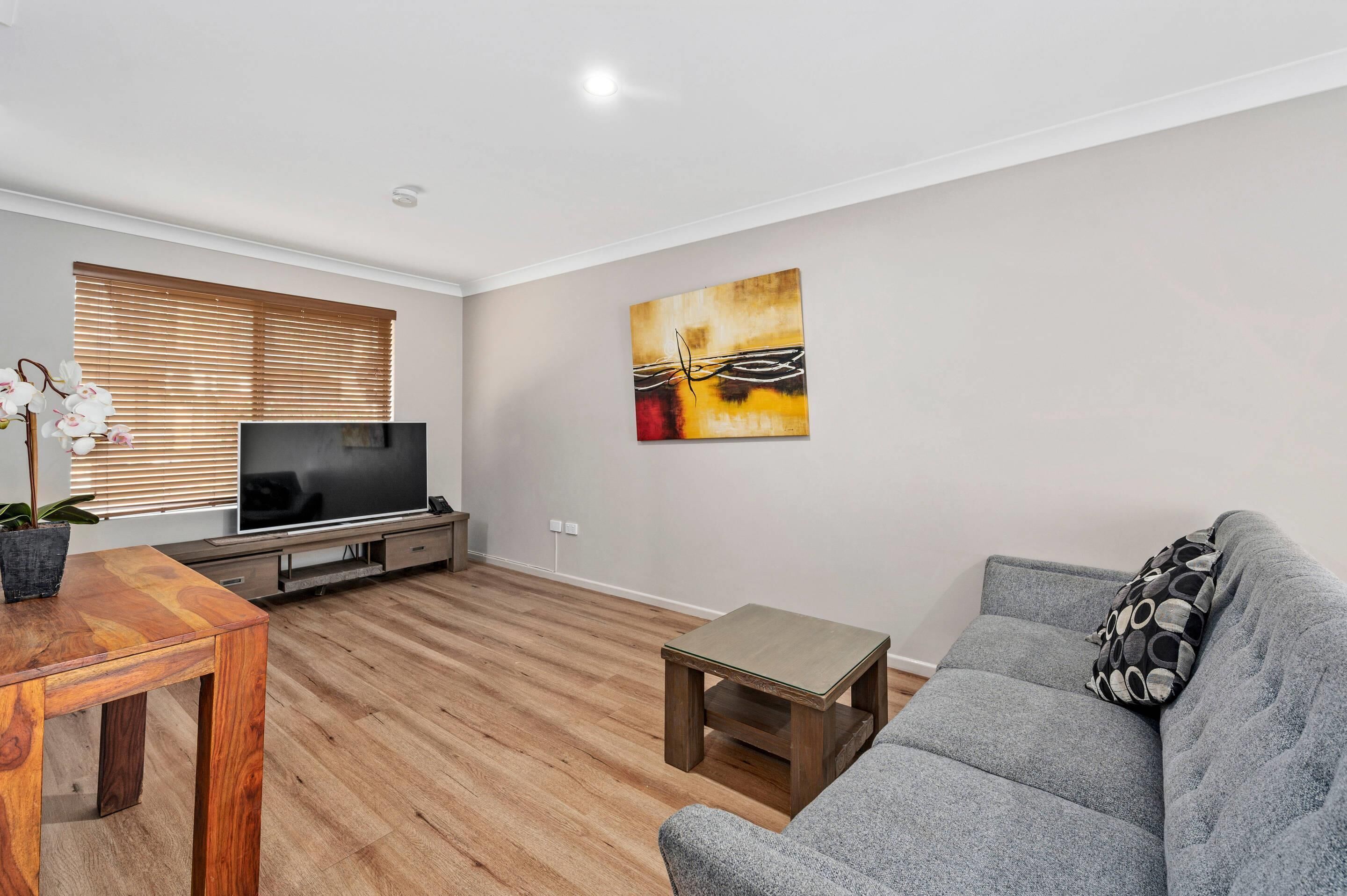 A modern living room with a flat-screen TV, a grey sofa, a wooden coffee table, and a painting on the wall.