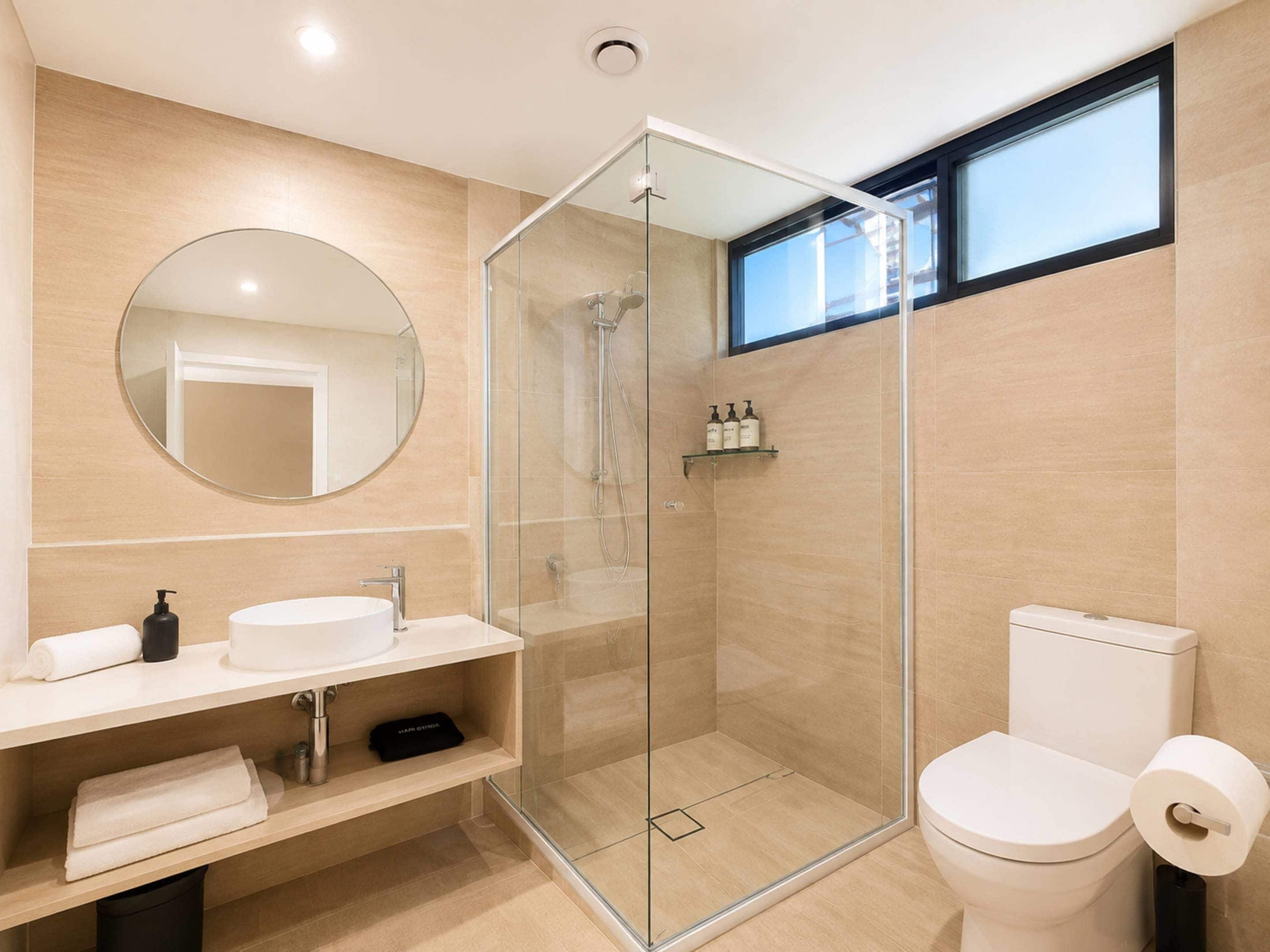 A modern bathroom with a glass-enclosed shower, a round mirror, a white sink, and a toilet.