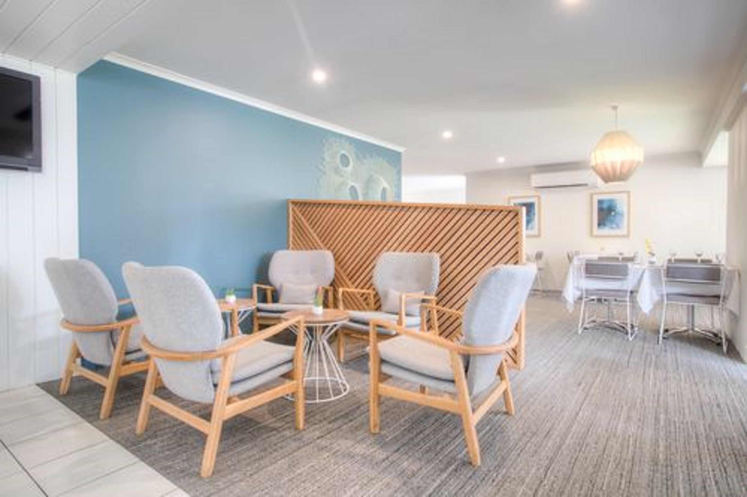 Una habitación de hotel moderna con una pared azul de acento, un panel de madera y un comedor con candelabro.