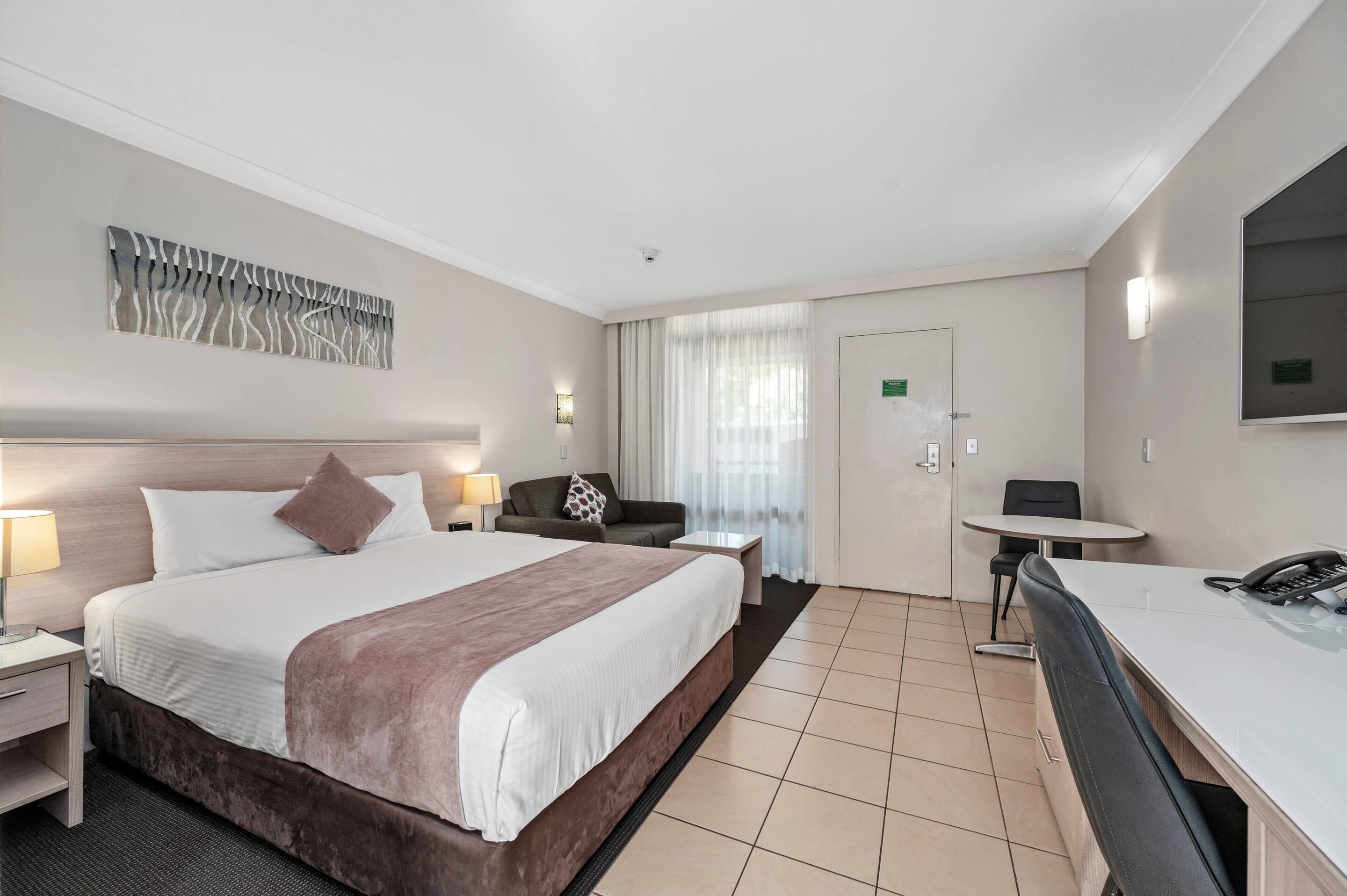 Habitación de hotel con cama, escritorio, silla, lámpara, teléfono y un cuadro en la pared.