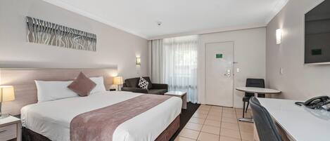Habitación de hotel con cama, escritorio, silla, lámpara, teléfono y un cuadro en la pared.